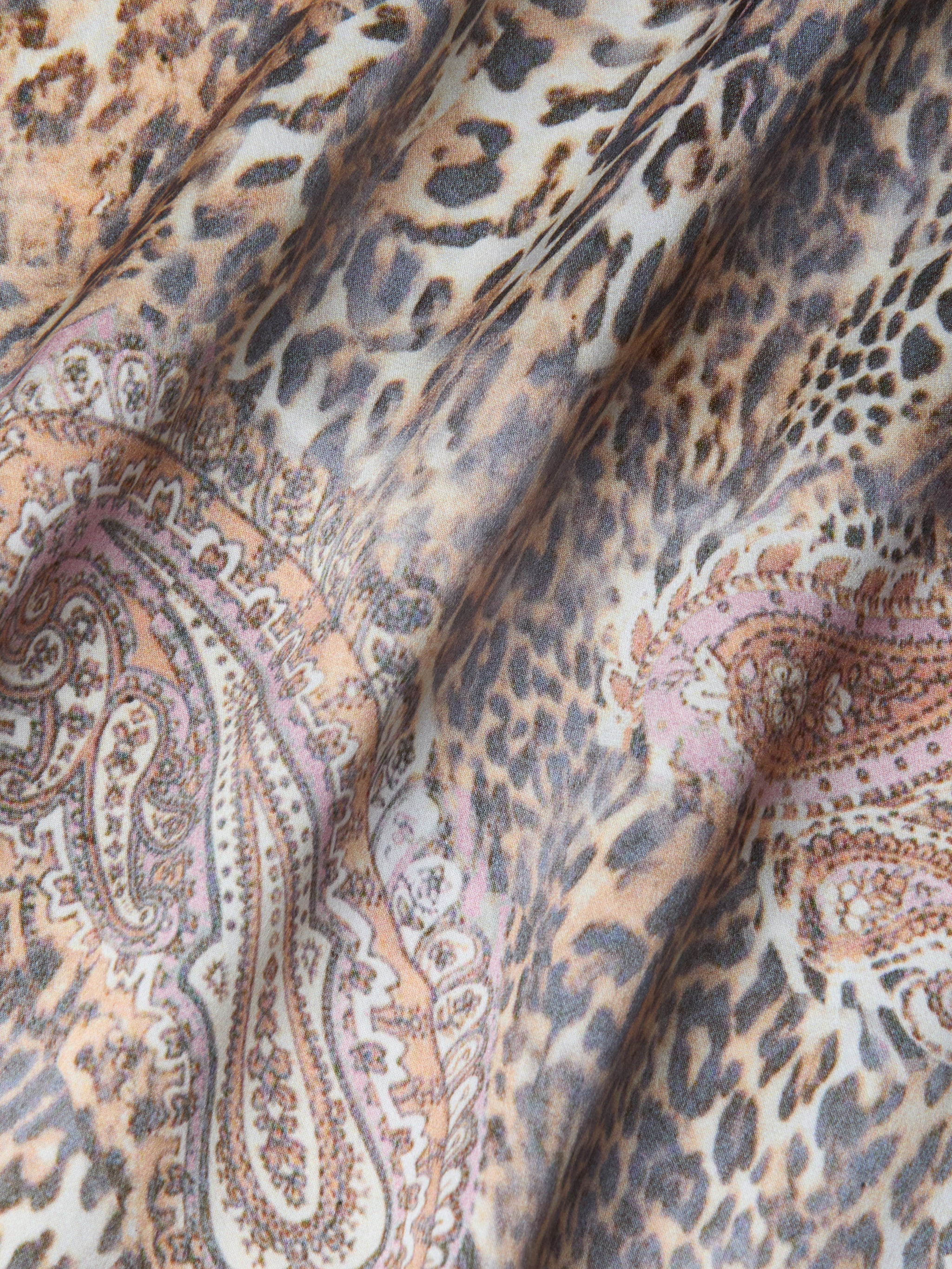 Gros plan sur le tissu de la robe en soie Charmaine, qui présente des motifs léopard et cachemire dans des tons beiges, bruns, noirs et rosés. Les plis souples créent des ombres et des textures, ce qui est idéal pour cette robe en soie coupée en biais et dotée de bretelles réglables.
