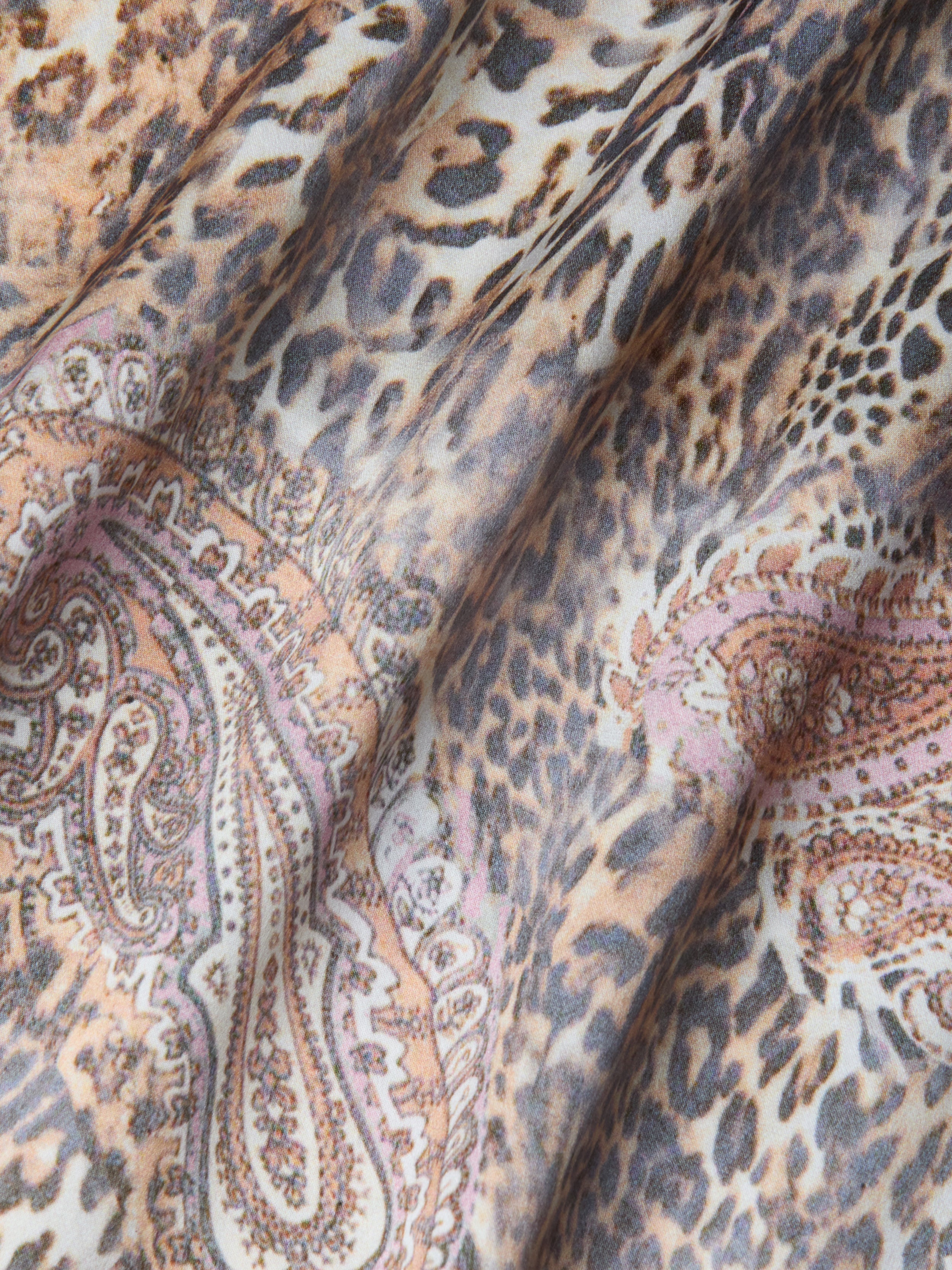 Gros plan sur le tissu de la robe en soie Charmaine, qui présente des motifs léopard et cachemire dans des tons beiges, bruns, noirs et rosés. Les plis souples créent des ombres et des textures, ce qui est idéal pour cette robe en soie coupée en biais et dotée de bretelles réglables.
