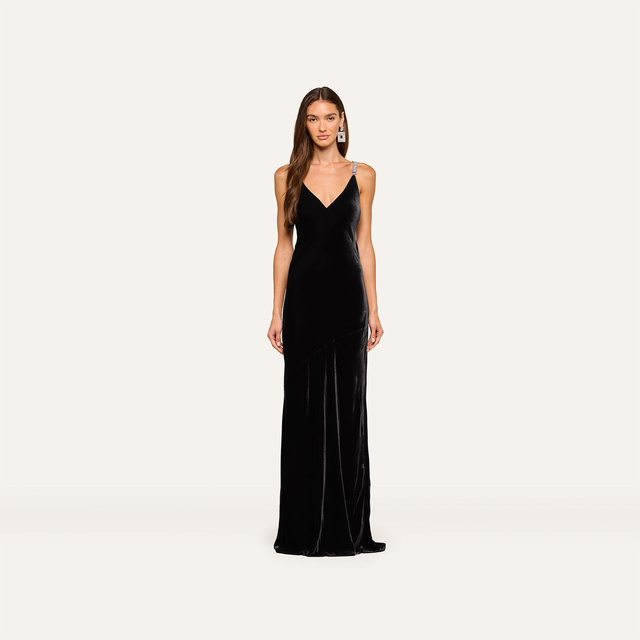 A woman faces forward in the Saint Velvet Gown—black velvet with thin crystal straps and a V-neckline—set against a plain light background.