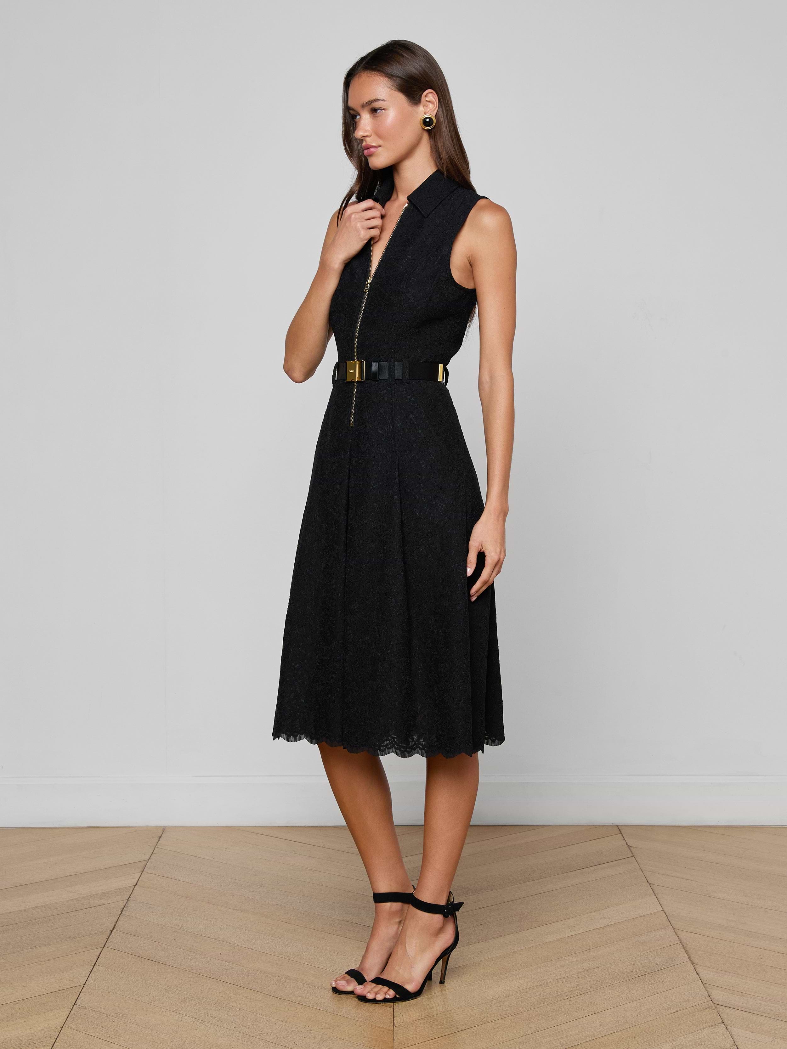 A woman wears the Kylo Lace Shirt Dress, a sleeveless black floral lace design paired with a wide belt and black high-heeled sandals, standing against a plain white background.