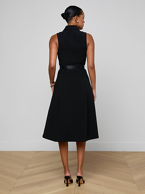 A woman with her hair in a bun stands on a light wooden floor, facing away from the camera. She is wearing the sleeveless, knee-length Kylo Shirt Dress paired with black high-heeled shoes.