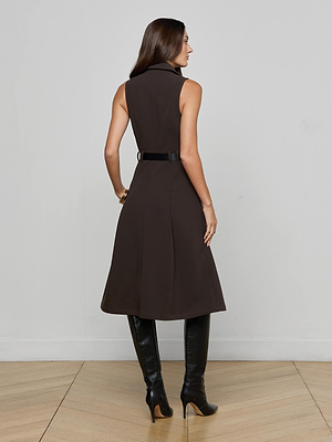 A woman with long brown hair stands with her back to the camera, wearing the L’AGENCE Kylo Shirt Dress and knee-high black boots on a light wooden floor against a plain light gray wall.