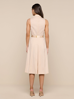 A woman with long brown hair stands facing away against a plain beige background, wearing the Kylo Poplin Shirt Dress—a sleeveless, belted light beige dress with a pleated skirt—paired with beige open-toe heels.