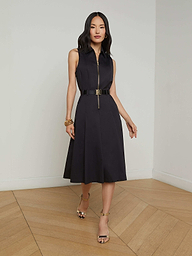 A woman in the Kylo Poplin Shirt Dress—a sleeveless black dress with a belt—stands against a plain white background, styled with gold heels and bracelets. Her hair is down, and her hands are relaxed at her sides. This versatile piece offers effortless style for any occasion, seamlessly taking you from desk to drinks.
