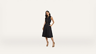 A woman stands confidently in a sleeveless black dress with a belted waist and pockets, wearing beige high-heeled sandals, against a plain white background.