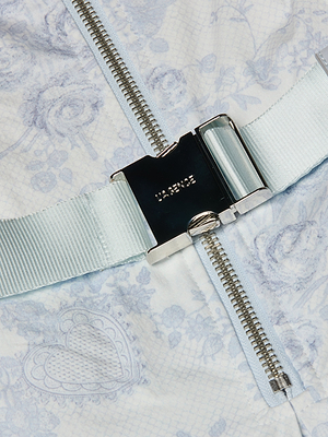 Close-up of the Kylo Shirt Dress in light blue lace print with floral and heart patterns, featuring a silver seatbelt-style buckle over a zipper—ideal for transitioning from desk to drinks.