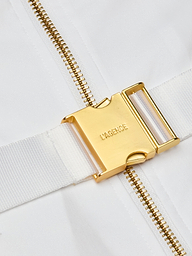 Close-up of a gold metal buckle engraved with LAGENCE on a white fabric strap, next to a gold zipper on a white background, highlighting the refined finish of the Kylo Poplin Shirt Dress crafted from organic cotton.