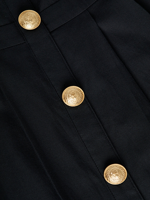 Close-up of a black fabric garment with three large, round gold buttons featuring an embossed design, arranged in a vertical line.