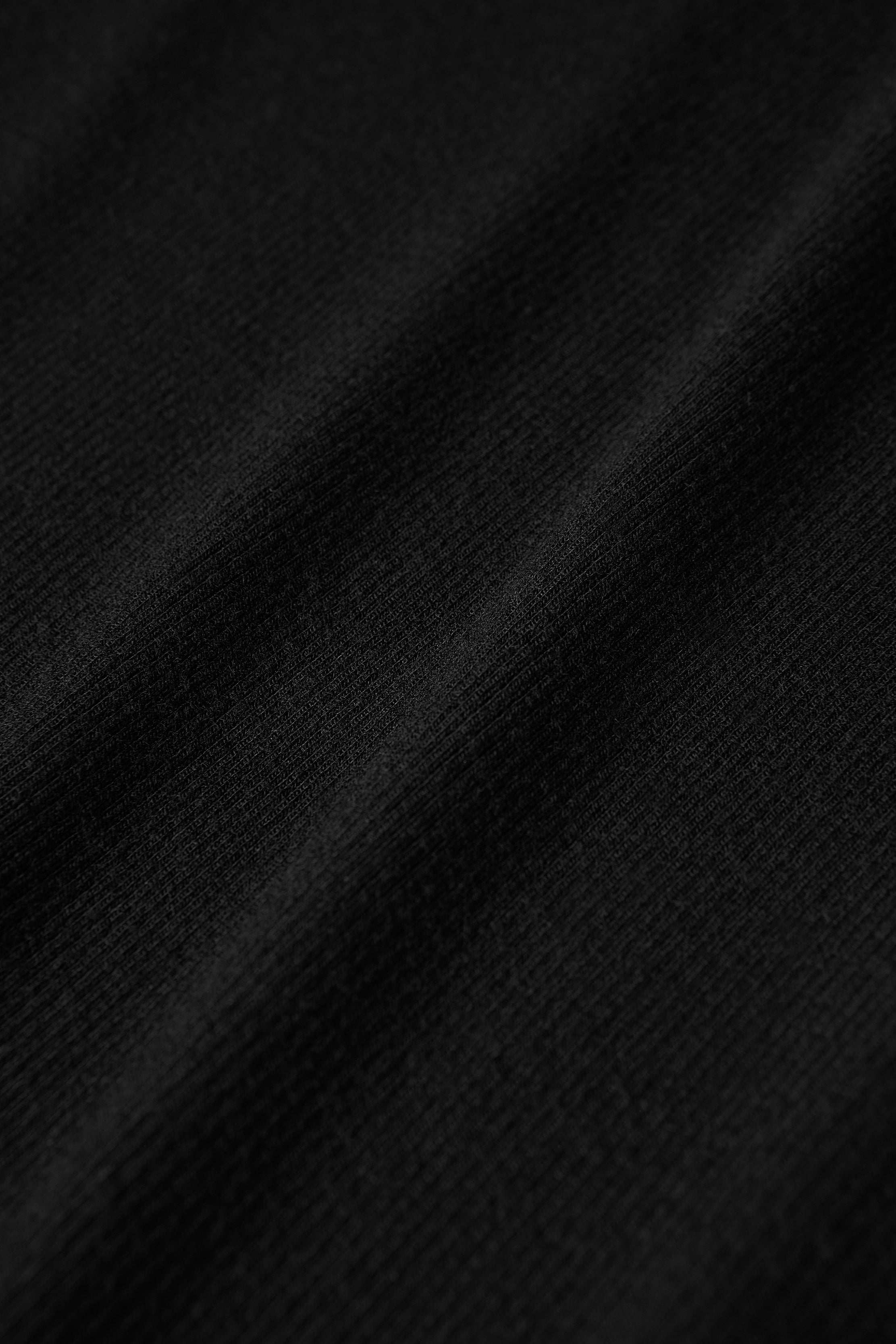 Close-up of a black microfiber modal jersey fabric with a soft texture and diagonal folds, showcasing fine weave details and subtle shadows across the surface—making it an ideal choice for the Voletta Turtleneck Knit Dress and a must-have essential for fall to winter.