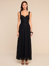 A woman stands against a plain background wearing the Sutton Lace Maxi Dress, a black lace maxi dress with a fitted bodice and scalloped neckline that offers a supportive fit. She completes her look with black high-heeled sandals.