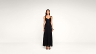 Woman standing against a plain background, wearing a long, sleeveless black lace dress with a scalloped neckline and black high-heeled sandals.