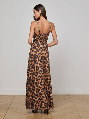 A woman stands with her back to the camera, wearing the L'AGENCE Sutton Beaded Strap Maxi Dress and black heels, set against a plain light wall and wooden floor.