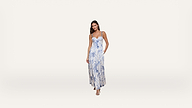A woman stands wearing a long, sleeveless white dress with blue floral patterns and strappy sandals against a plain white background.