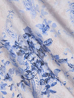 Close-up of the Sutton Beaded Strap Gown’s light fabric, showcasing delicate lace with blue floral and paisley print on white—ideal for spring/summer. Intricate flowers and leaves add an elegant, decorative touch to this gown.