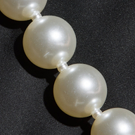 A close-up of a pearl necklace with round white pearls resting on the Sutton Maxi Dress.