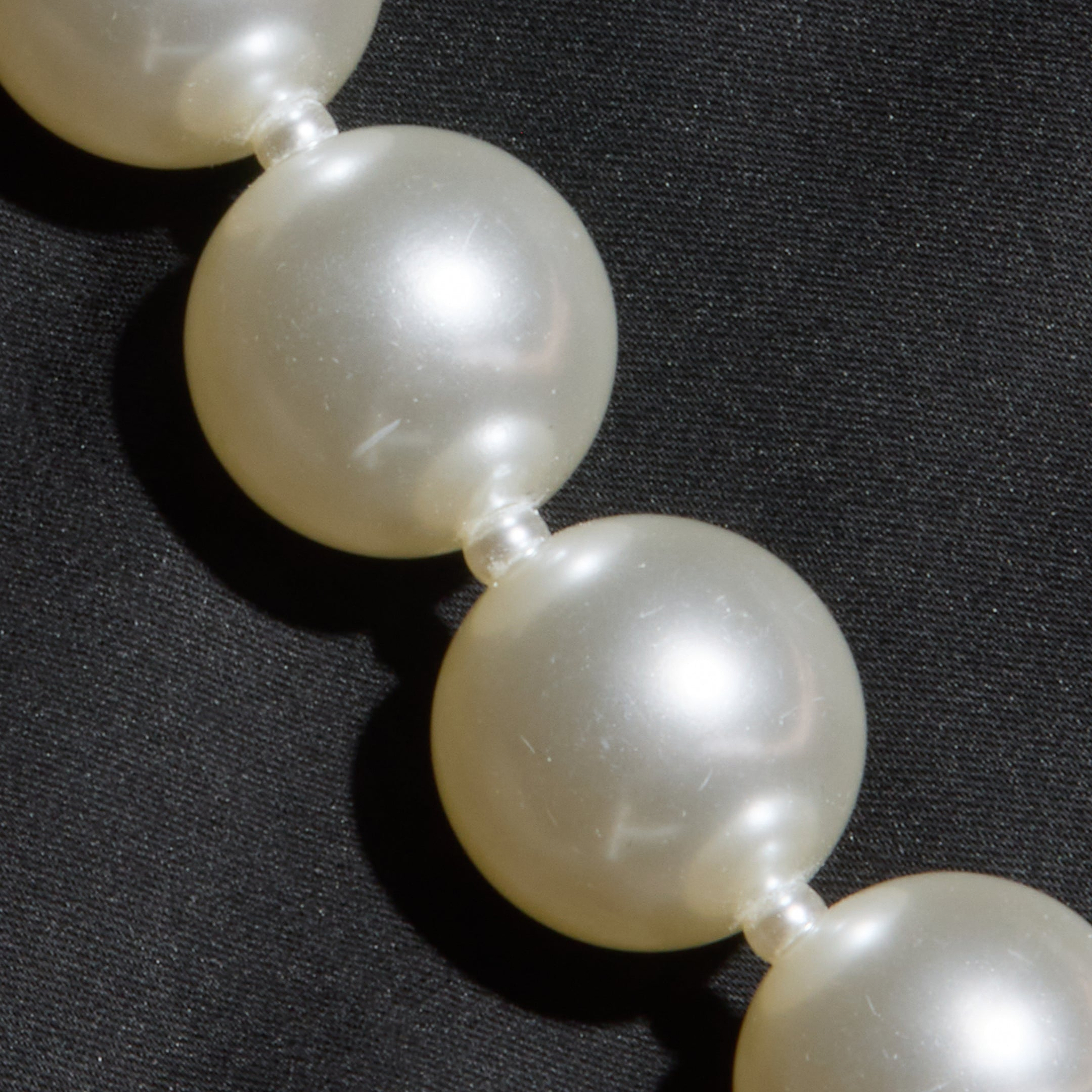 A close-up of a pearl necklace with round white pearls resting on the Sutton Maxi Dress.