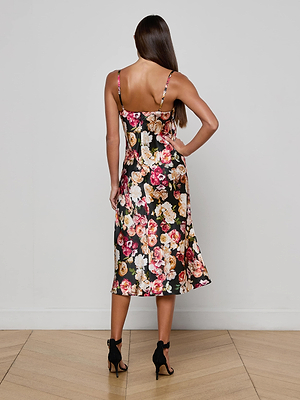 A woman with long straight hair wears the L'AGENCE Solay Silk Slip Dress, standing on a wooden floor with her back to the camera against a plain light gray wall.
