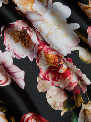 A close-up of colorful pink, white, and red peony flowers decorates the smooth black fabric of the Solay Silk Slip Dress by L'AGENCE, with gentle folds that enhance the floral pattern’s depth and elegant texture.