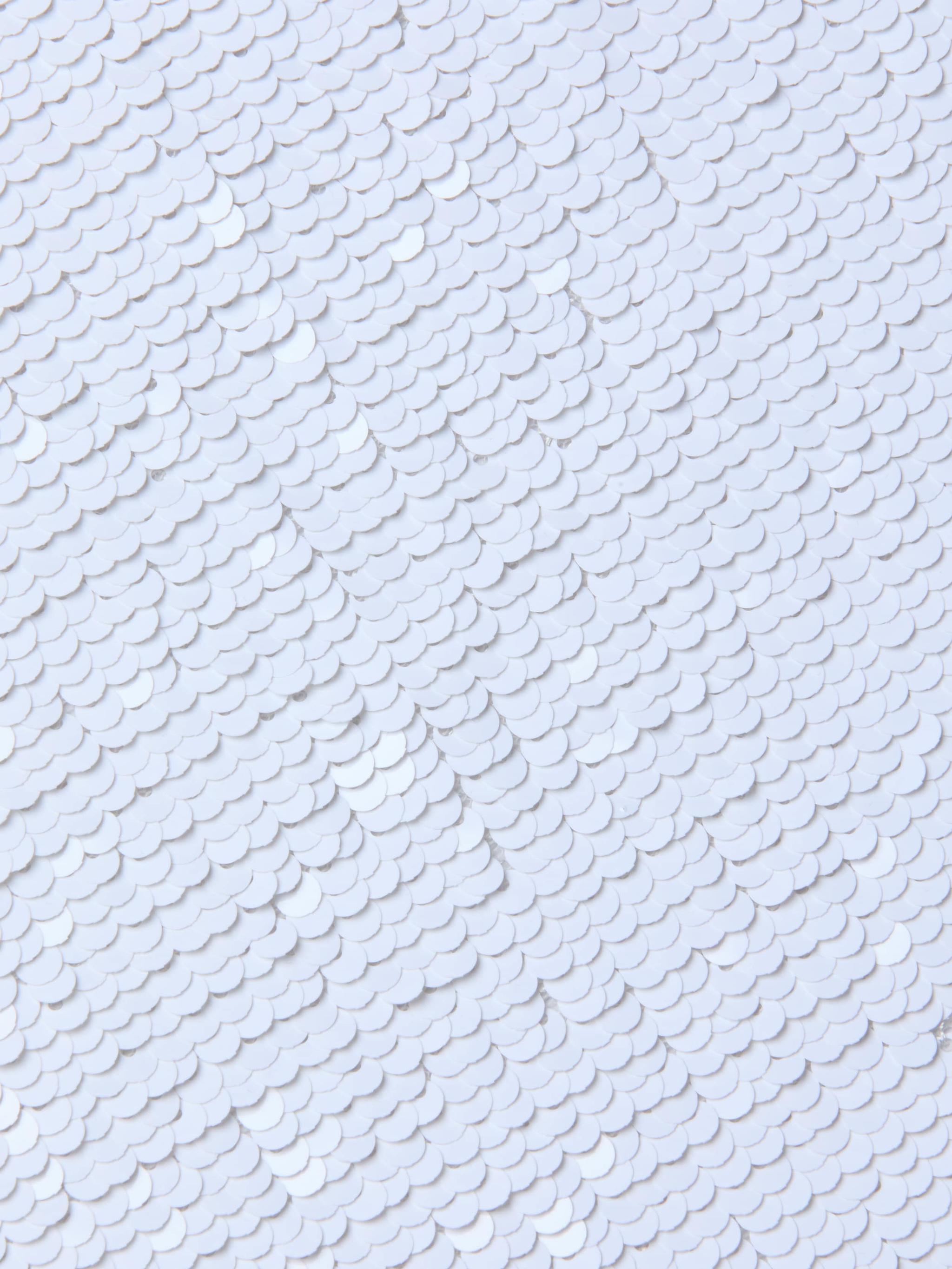 Close-up of overlapping white sequins on the Lilith Sequin Dress, creating a textured, shiny surface with a subtle fish-scale pattern on this fitted party piece.