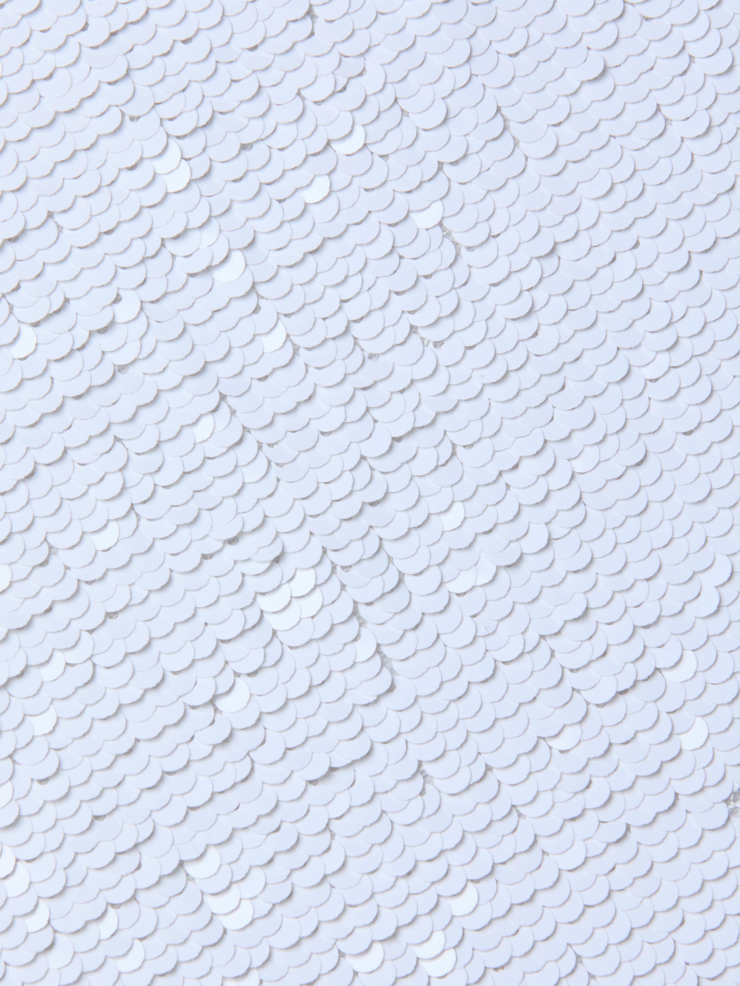 Close-up of overlapping white sequins on the Lilith Sequin Dress, creating a textured, shiny surface with a subtle fish-scale pattern on this fitted party piece.
