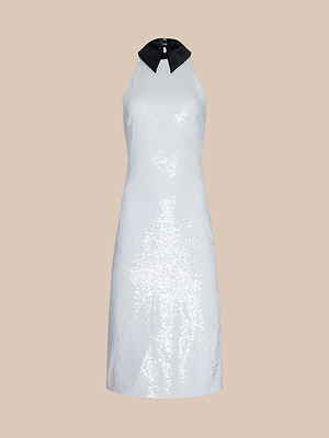The Lilith Sequin Dress is a sleeveless, knee-length white fitted dress with sparkling sequins and a bold black poplin collar, perfect for parties. Shown on a plain beige background.