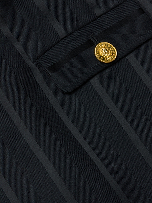 Close-up of the Helen Mini Dress by L'AGENCE, showing dark pinstriped fabric with a flap and a single round gold button featuring a detailed decorative design.