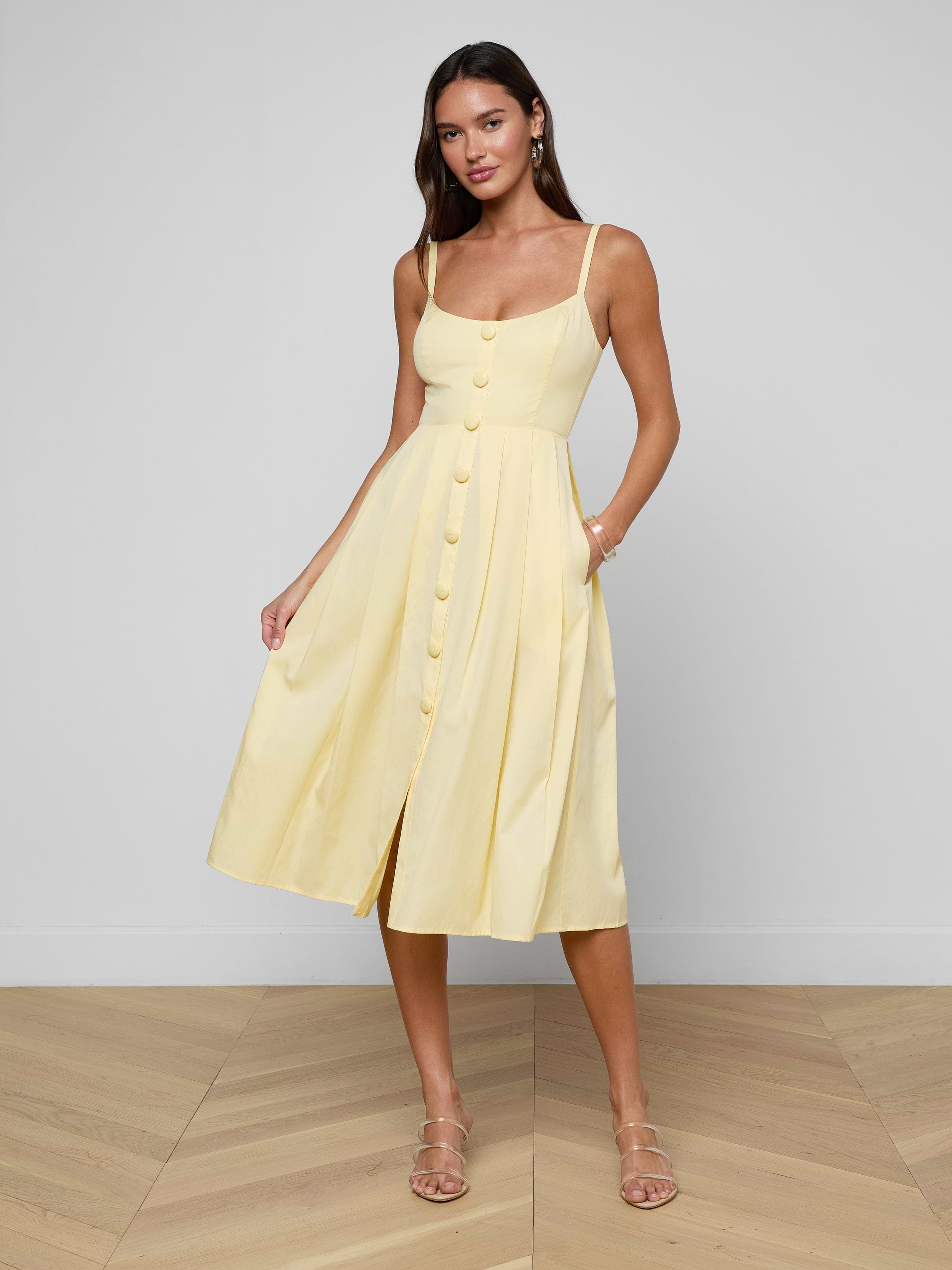 Wearing the Reanne Midi Dress, a woman stands against a plain white background. The light yellow sleeveless dress features thin straps, convenient pockets, and a smocked back for added comfort.