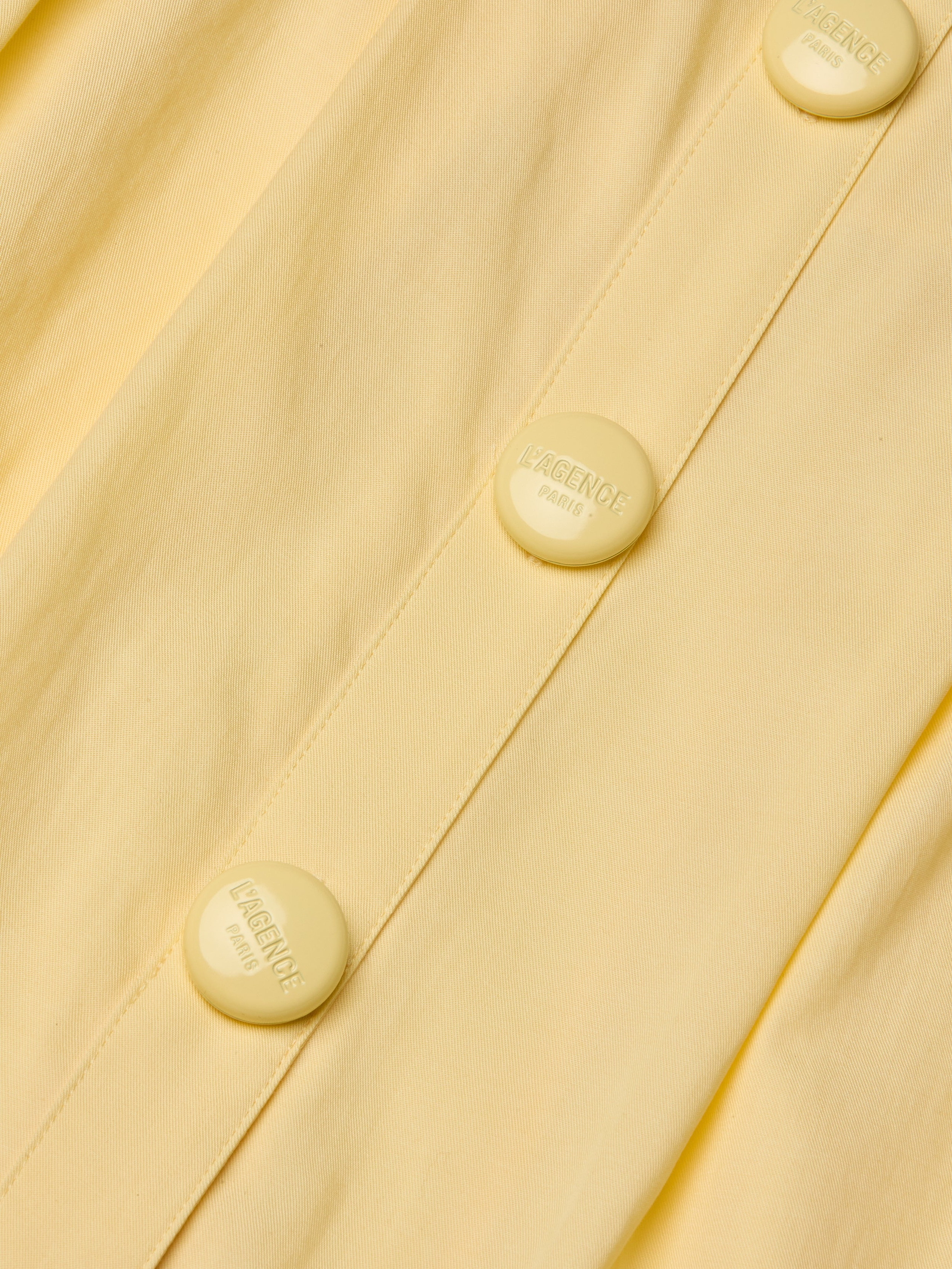 Close-up of the Reanne Midi Dress in yellow poplin, featuring matching buttons embossed with the words LAGENCE PARIS. The image highlights the fabric’s texture and detailed button design.