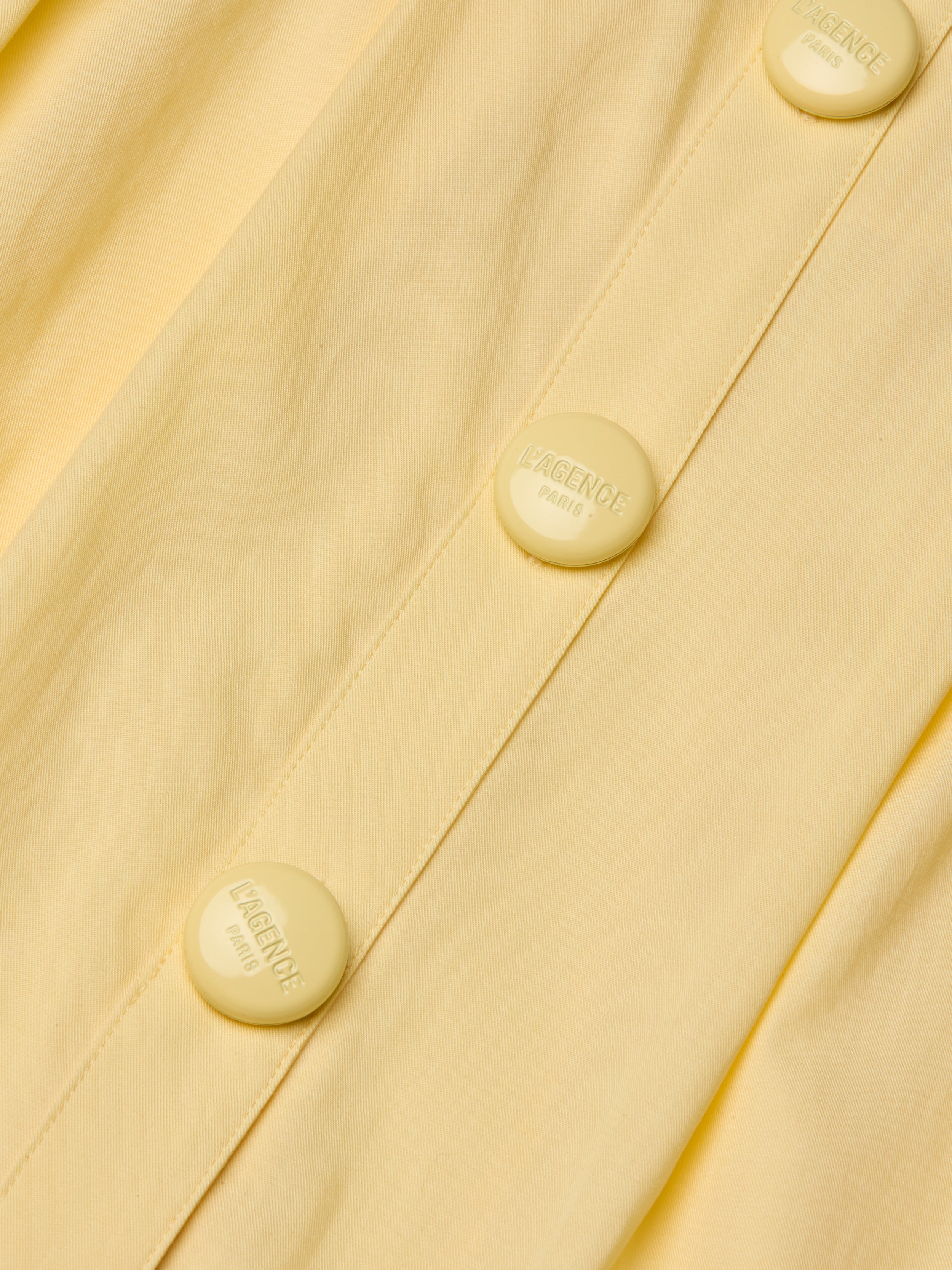 Close-up of the Reanne Midi Dress in yellow poplin, featuring matching buttons embossed with the words LAGENCE PARIS. The image highlights the fabric’s texture and detailed button design.