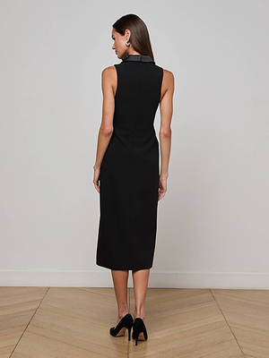 A woman stands indoors with her back turned, wearing the L'AGENCE Catherine Tuxedo Midi Dress and black heels. The room features light walls and wooden floors.