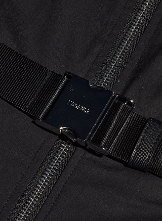 Close-up of a black metal buckle fastened over a dark zipper, with black fabric and webbing straps in the background—bold hardware inspired by statement belt details designed for the Kolton Dress.