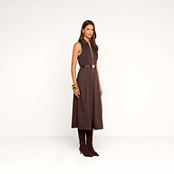 A woman stands against a plain white background wearing the Kolton Dress—a sleeveless, dark brown cotton-blend poplin midi dress—styled with gold bangles and knee-high brown boots.