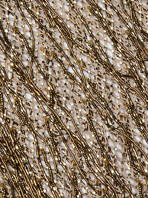 Close-up of the Gracelynn Beaded Fringe Dress, featuring artisanal craftsmanship with intricate antique gold bugle beads and sequins arranged in wavy, diagonal lines on sheer white fabric for a luxurious, sparkling texture.
