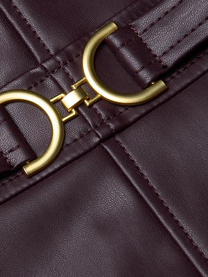 Close-up of the Halia Vegan Leather Dress by L'AGENCE in burgundy, showcasing visible stitching and a circular gold-tone buckle—an elegant accent for a form-fitting silhouette.