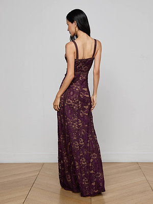 A woman with long dark hair stands with her back to the camera in a minimalist room, wearing the sleeveless, floor-length Laynie Lace Maxi Dress. The space features light wood flooring and a plain gray wall.
