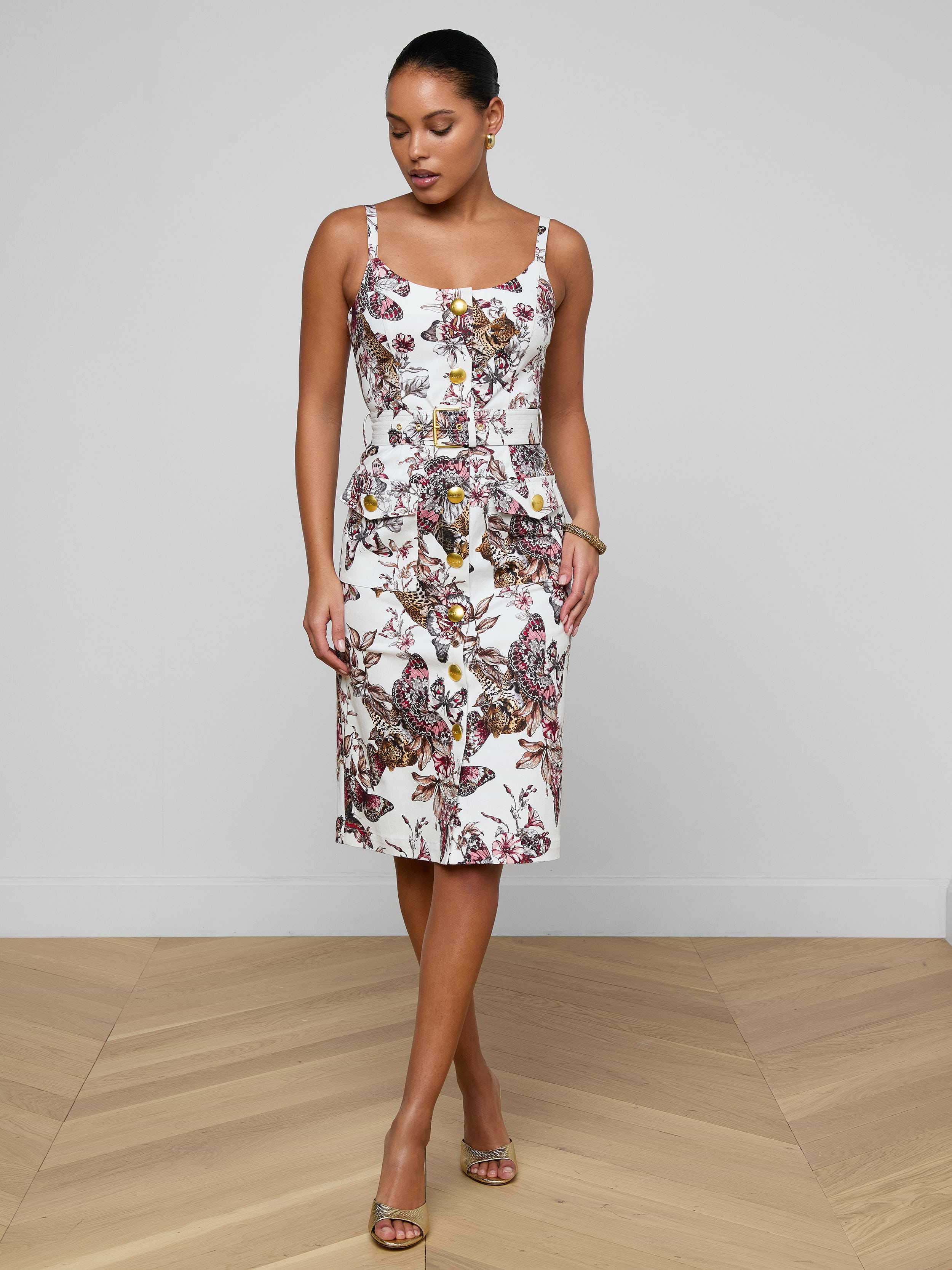 Wearing the Ida Dress—a sleeveless, fitted stretch cotton design adorned with a colorful floral pattern—a woman stands against a plain white background, looking down with her hands in her pockets.