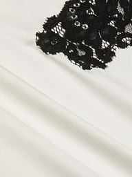 Close-up of black floral lace fabric layered over smooth, white silk charmeuse, showcasing the striking contrast in textures and colors that evoke the elegance of the Fenna Silk Lace Dress.