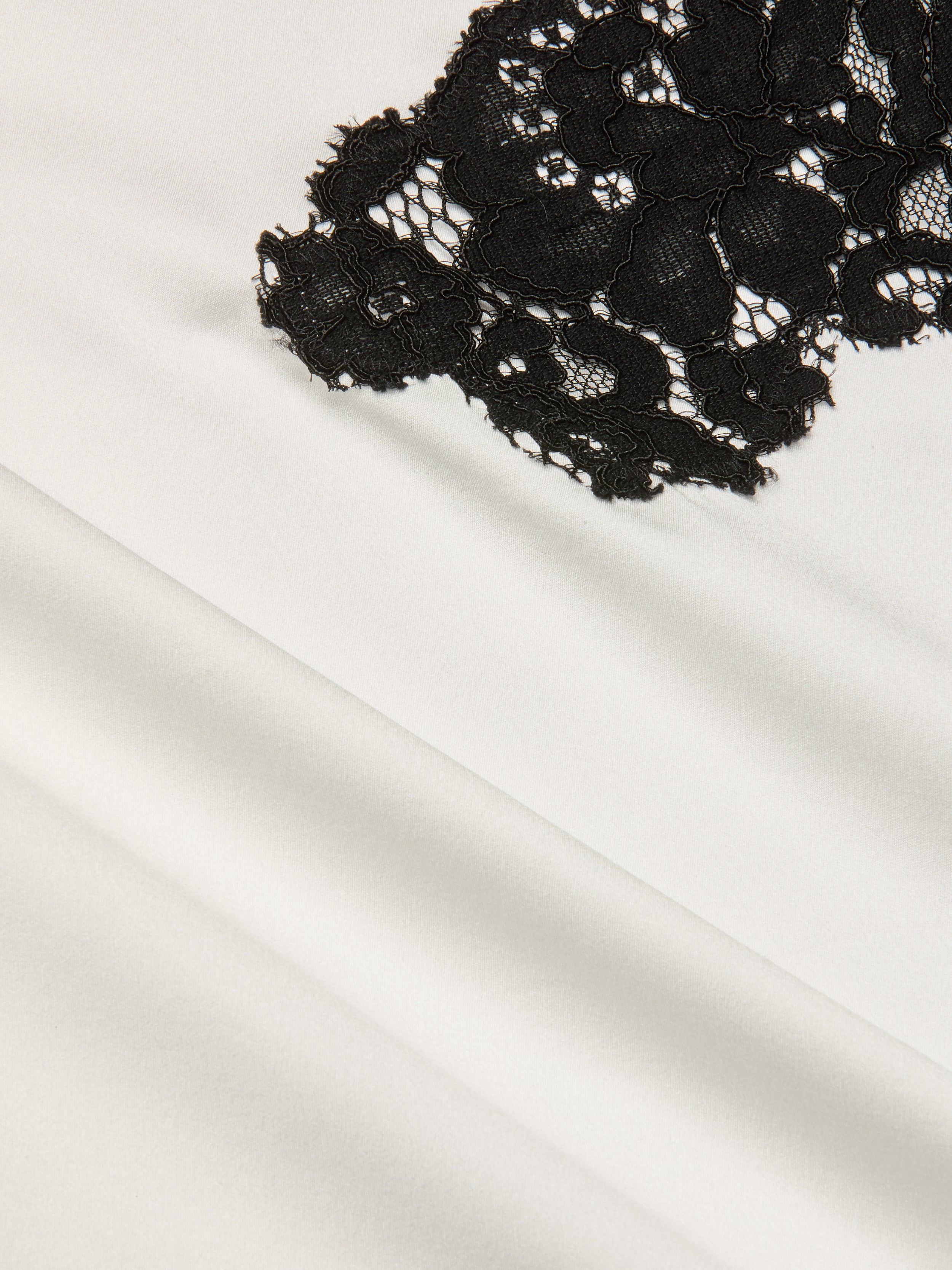 Close-up of black floral lace fabric layered over smooth, white silk charmeuse, showcasing the striking contrast in textures and colors that evoke the elegance of the Fenna Silk Lace Dress.