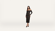 Woman wearing a black off-shoulder, long sleeve lace dress and black heels stands against a plain white background, facing forward with a neutral expression.