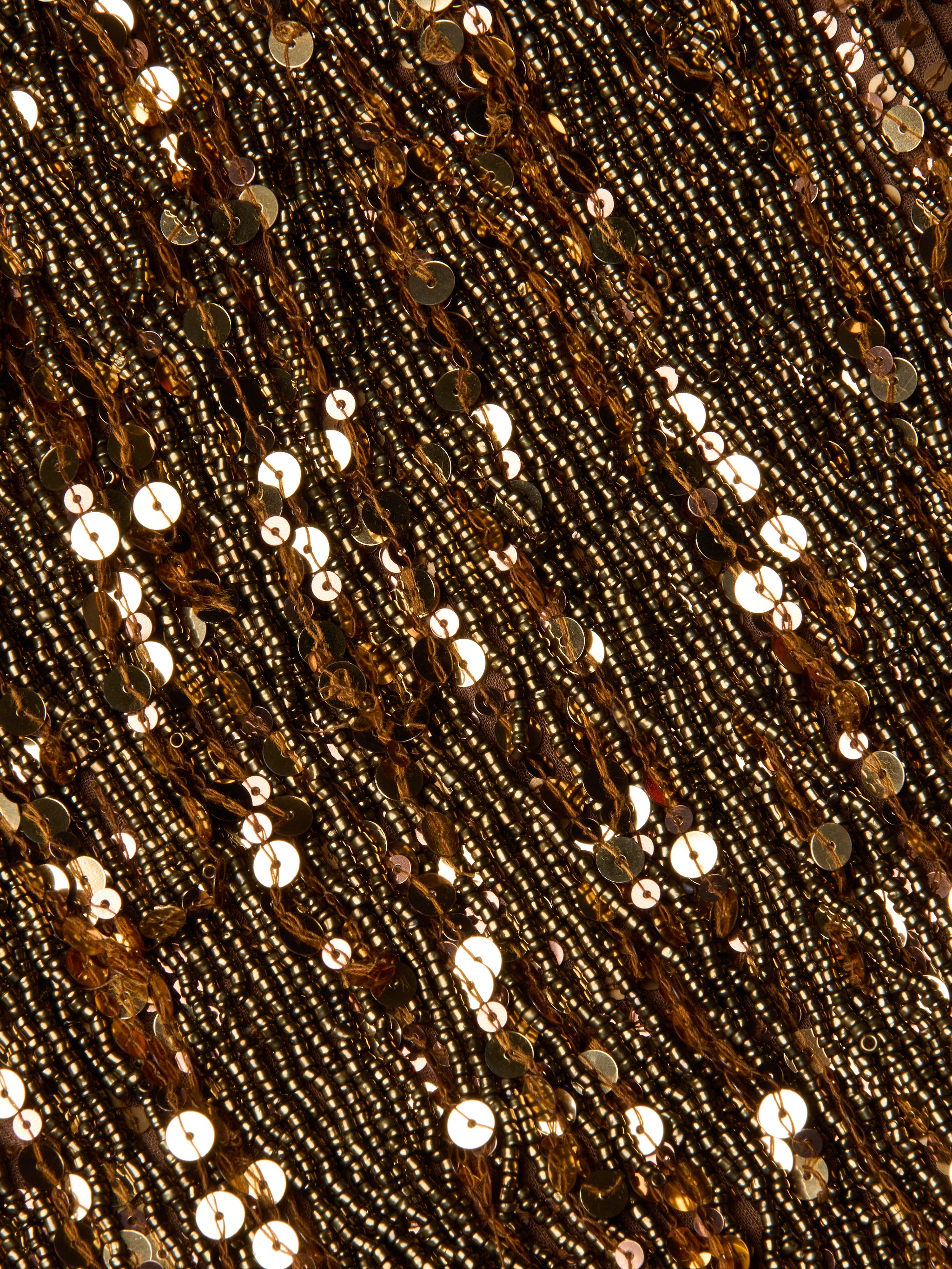 Close-up of the Noella Sequin Fringe Dress, featuring gold sequins and beads shimmering on fabric in dense, wavy horizontal patterns with fringe embellishments, creating a rich, textured, and reflective surface.
