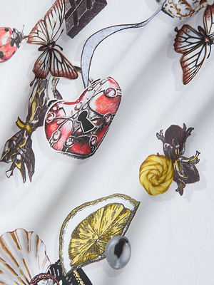 The Sayla Silk Gown features a whimsical white fabric with detailed butterflies, a red heart-shaped lock, yellow flowers, chocolate pieces, a lemon slice, and pearls—perfect for an event-ready look.