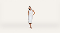 Woman standing against a plain white background, wearing a sleeveless white midi dress with front buttons, a halter neckline, belted waist, and white strappy heels. She has long dark hair and one hand on her hip.