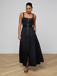 A woman wearing the Rima Maxi Dress—a sleeveless black maxi dress with a belted waist crafted from stretch poplin—paired with black heels stands against a plain light background, looking down with one hand touching the skirt.