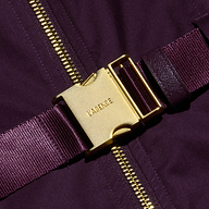 An adjustable belt made from a dark purple strap, featuring a gold metal buckle engraved with LAGENCE, accents the Rima Dress, shown on matching fabric beside a gold zipper.