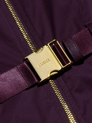 Close-up of a gold buckle engraved with LAGENCE, attached to a purple stretch poplin strap and fabric, alongside a gold zipper—an elegant detail that elevates the adjustable belt of the Rima Dress.