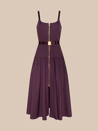 The Rima Dress, displayed on a beige background, is a sleeveless, knee-length plum piece crafted from stretch poplin and features a front gold zipper, fitted bodice, flared skirt, and a matching adjustable belt with a gold buckle.