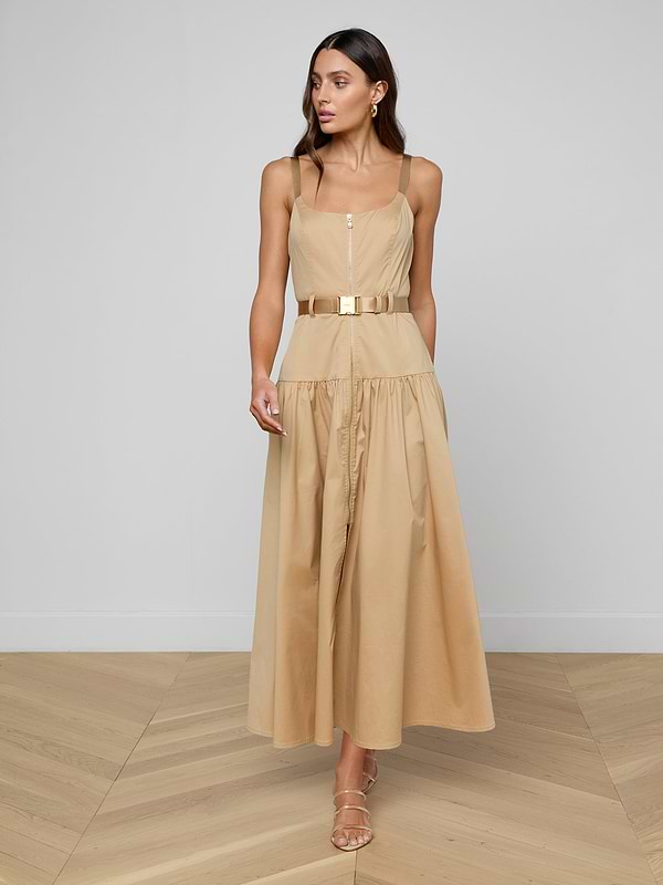 Woman in the Rima Maxi Dress— a neutral tan stretch poplin, sleeveless, belted midi dress — paired with sandals and standing against a plain white background.