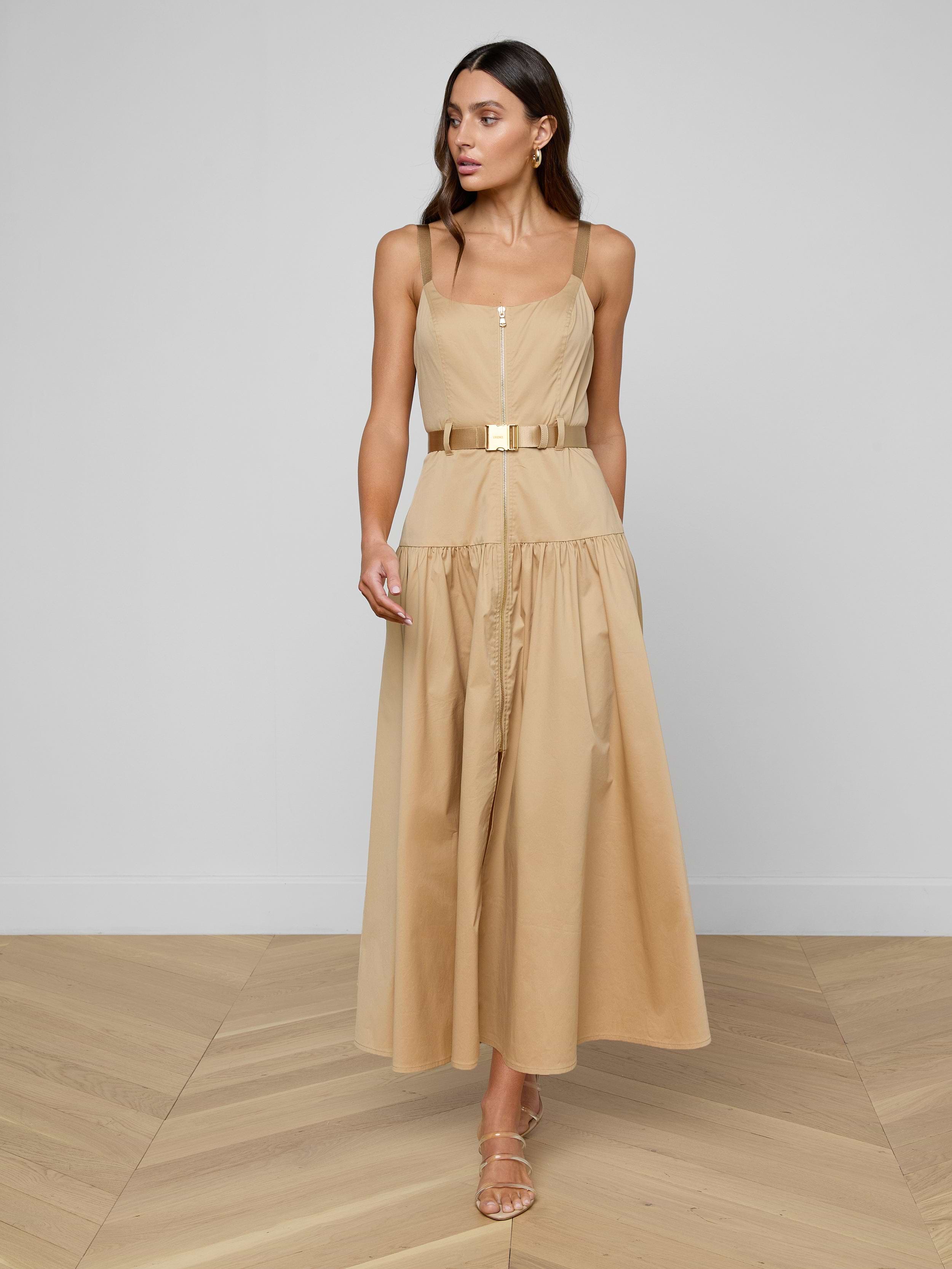 Woman in the Rima Maxi Dress— a neutral tan stretch poplin, sleeveless, belted midi dress — paired with sandals and standing against a plain white background.