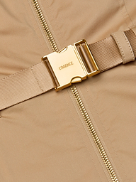 Close-up of the Rima Maxi Dress in a neutral tan stretch poplin, showcasing a gold metal buckle engraved with LAGENCE and a beige zipper running vertically beside it. The buckle is attached to a matching fabric strap.