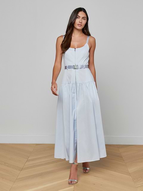 Wearing the Rima Maxi Dress—a pale blue, sleeveless, belted stretch poplin maxi dress—a woman paired with silver heels stands against a plain white background.